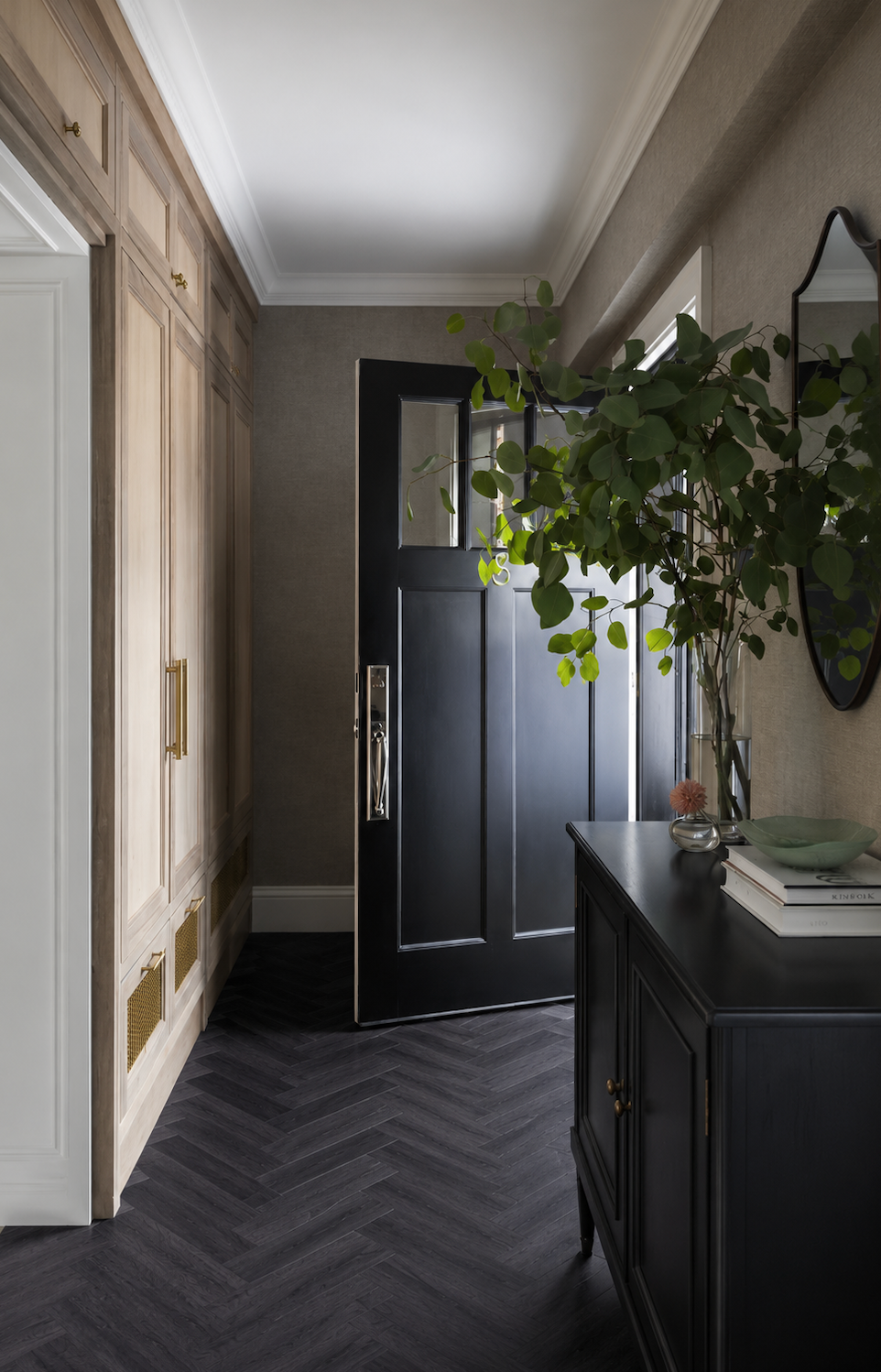Black Ash Herringbone Luxury Click Vinyl Flooring in a modern entrance hallway, showcasing dark wood-effect herringbone vinyl flooring with realistic oak grain texture and deep charcoal tones. Waterproof click vinyl flooring installed in a high-traffic hallway, paired with fitted storage, a black front door and contemporary interior design.