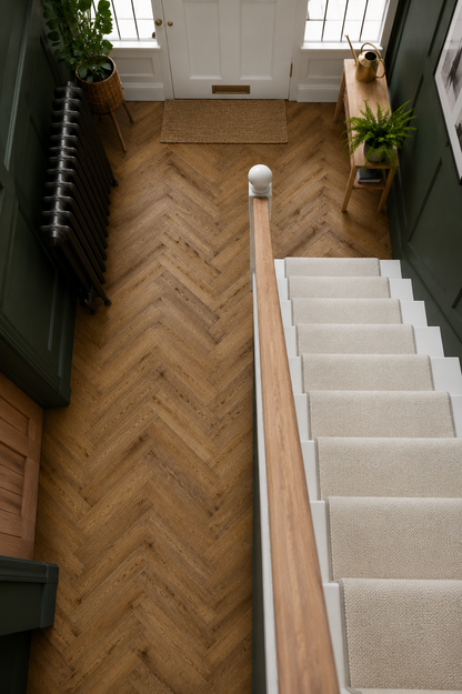 Sugar Oak Herringbone Luxury Click Vinyl Flooring in a modern hallway, showcasing oak-effect herringbone vinyl flooring with realistic wood grain detail and warm natural tones. Waterproof click vinyl flooring installed in a high-traffic entranceway, paired with dark green wall panelling, staircase and contemporary home décor.
