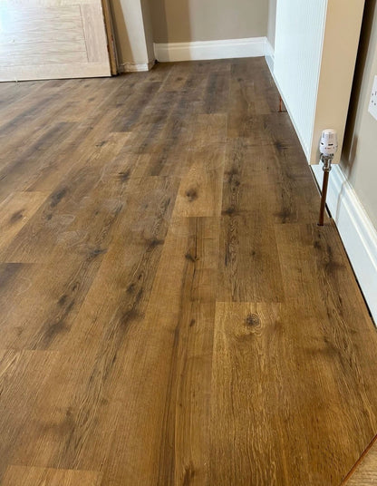 Brown wood-look laminate or vinyl plank flooring installed in a room, showing the grain and texture of the planks.