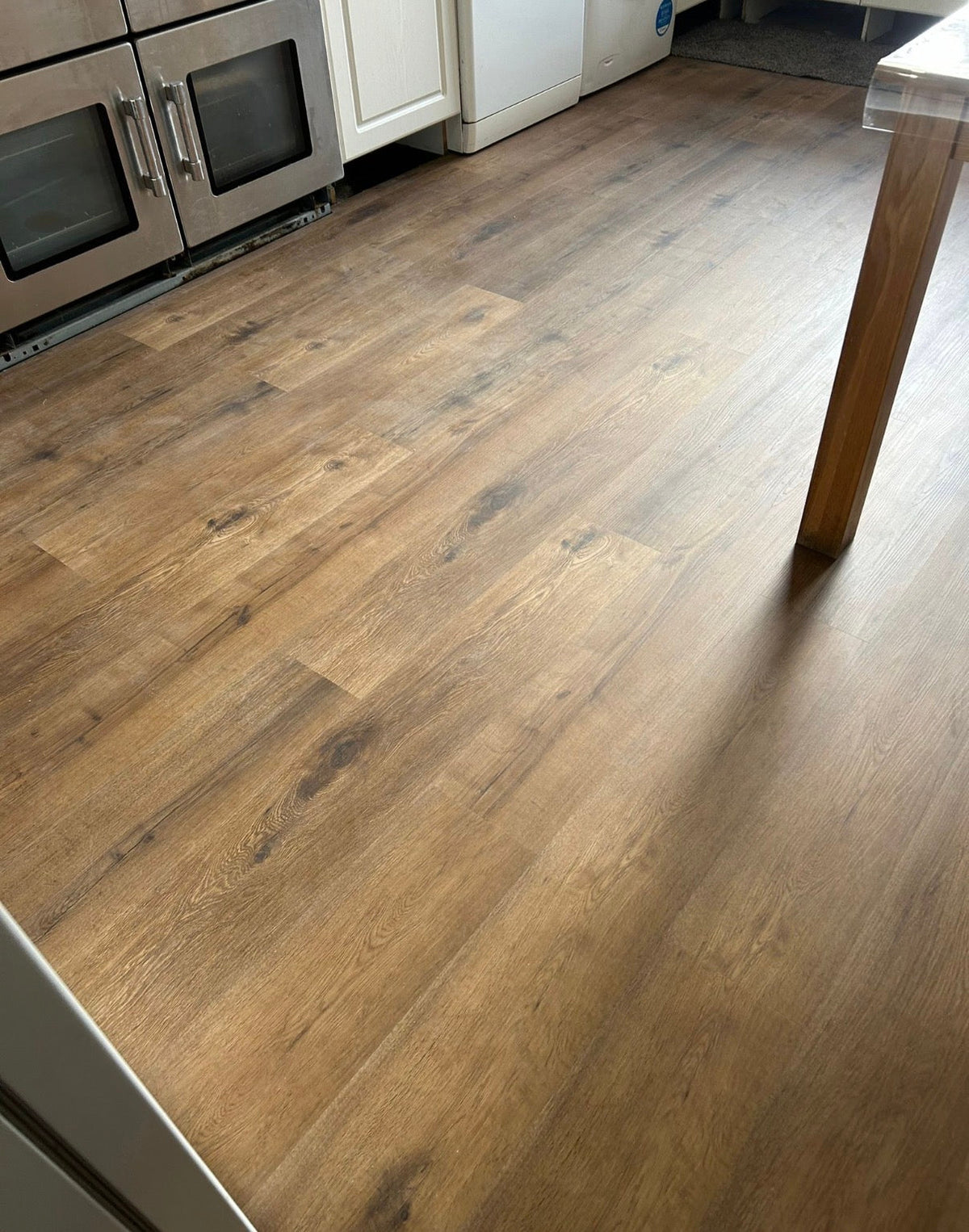 Brown wood-look laminate or vinyl plank flooring installed in a kitchen, showing the grain texture and color variation.