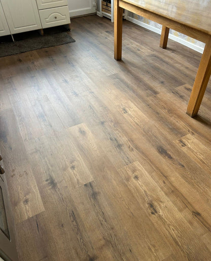 Light brown wood-look laminate flooring installed in a room with a wooden dining table and white cabinets.