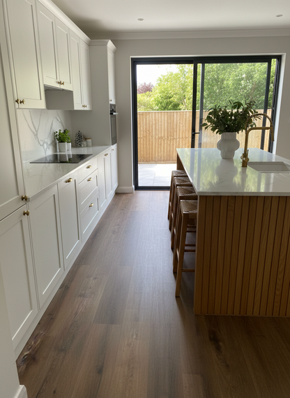 Sugar Oak Luxury Click Vinyl Flooring 5mm installed in a contemporary kitchen, showcasing warm honey oak wood-effect planks with authentic grain detailing and a realistic matt finish, beautifully complementing white cabinetry, a timber island and large patio doors.